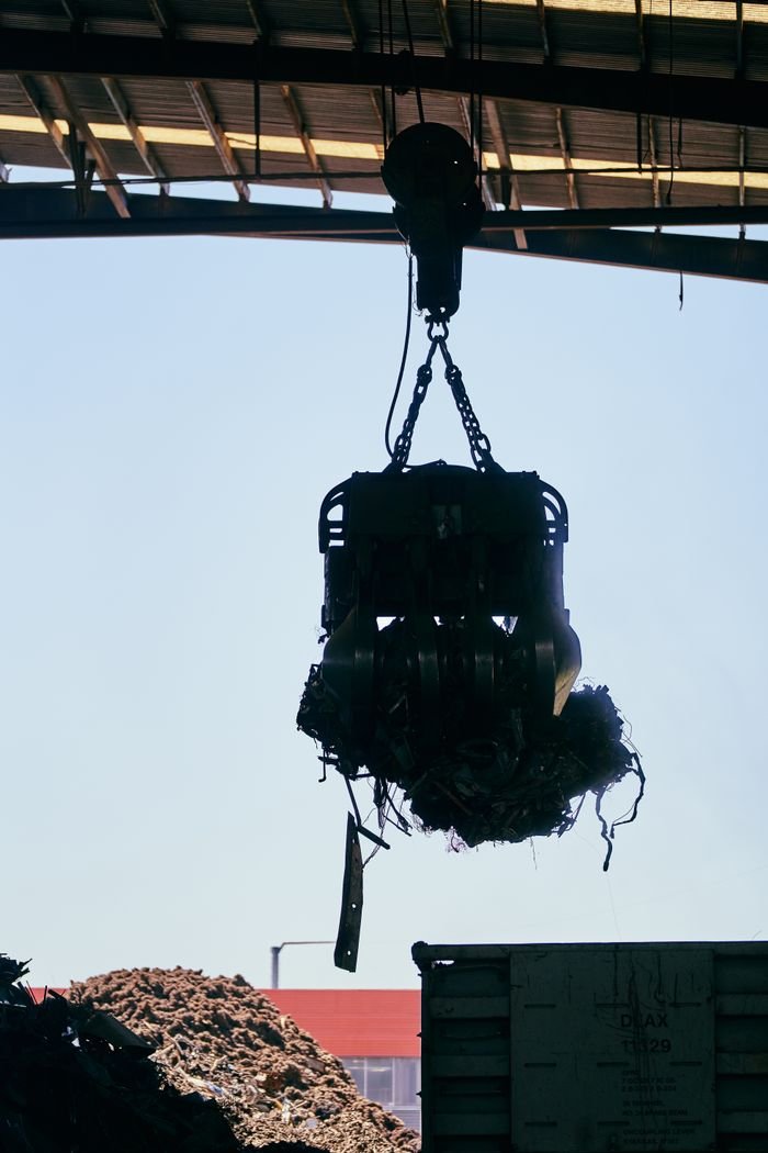 Silhouette of industrial crane lifting metal debris in a warehouse.