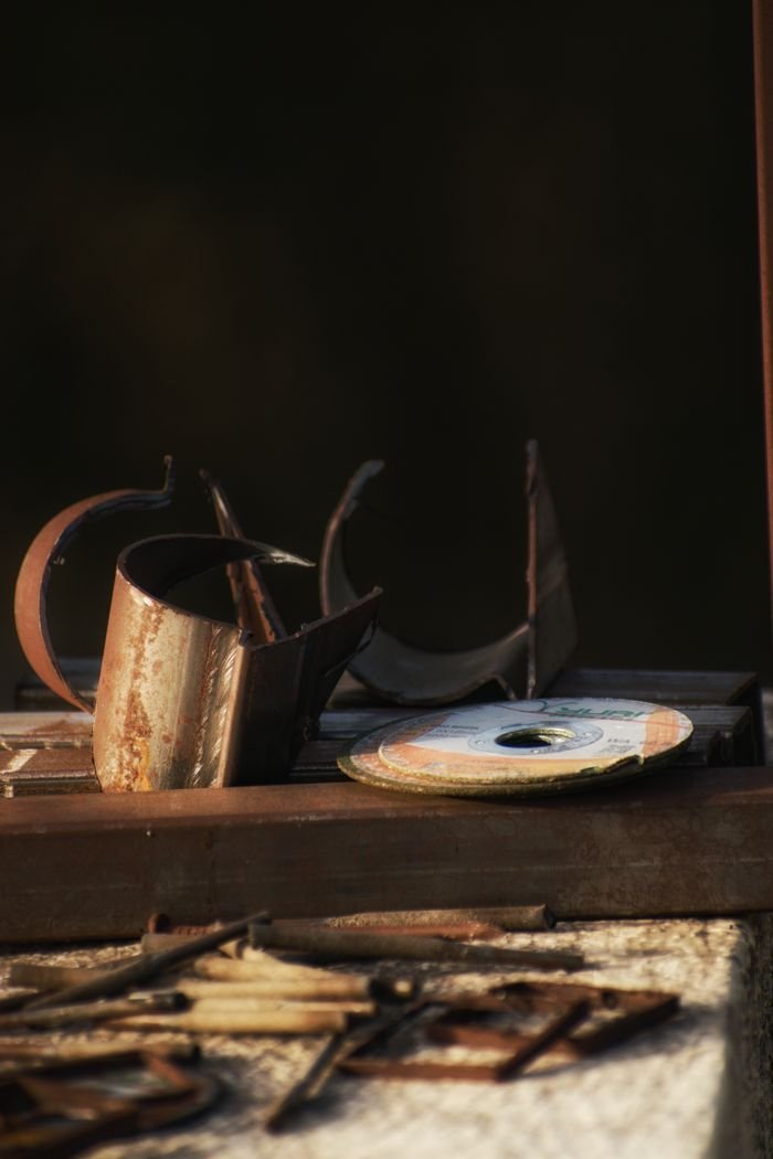 Used cutting discs and weathered metal details placed on table near pile of rusty nails in old workshop